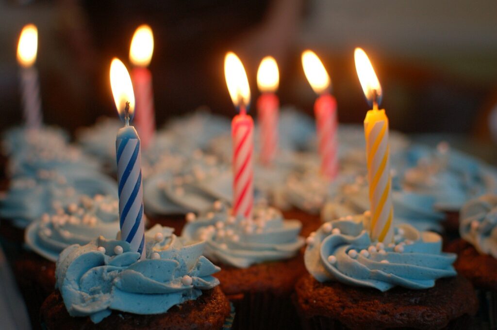 Chocolate cupcakes with blue frosting, lit candles, and white sprinkles, perfect for a birthday celebration.