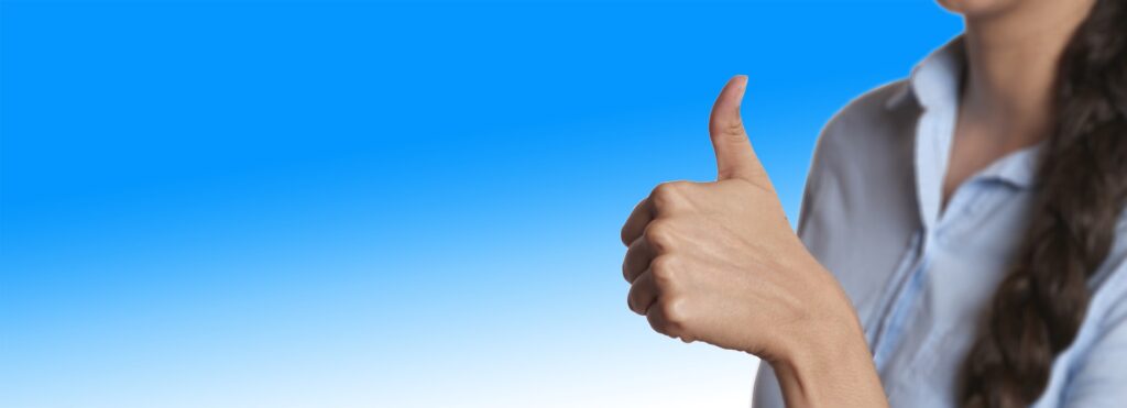 Person giving thumbs up against a clear blue sky background, wearing a light blue shirt.