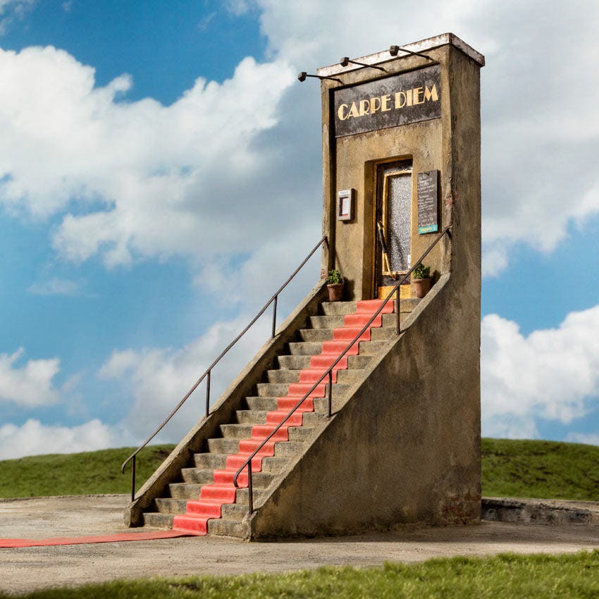 Concrete stairs with red carpet lead to a door labeled Carpe Diem under a blue sky with clouds.