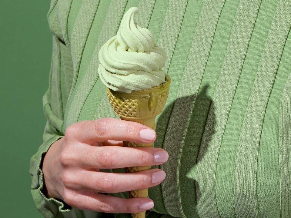Person in green holds a light green ice cream cone with a decorative gold base.