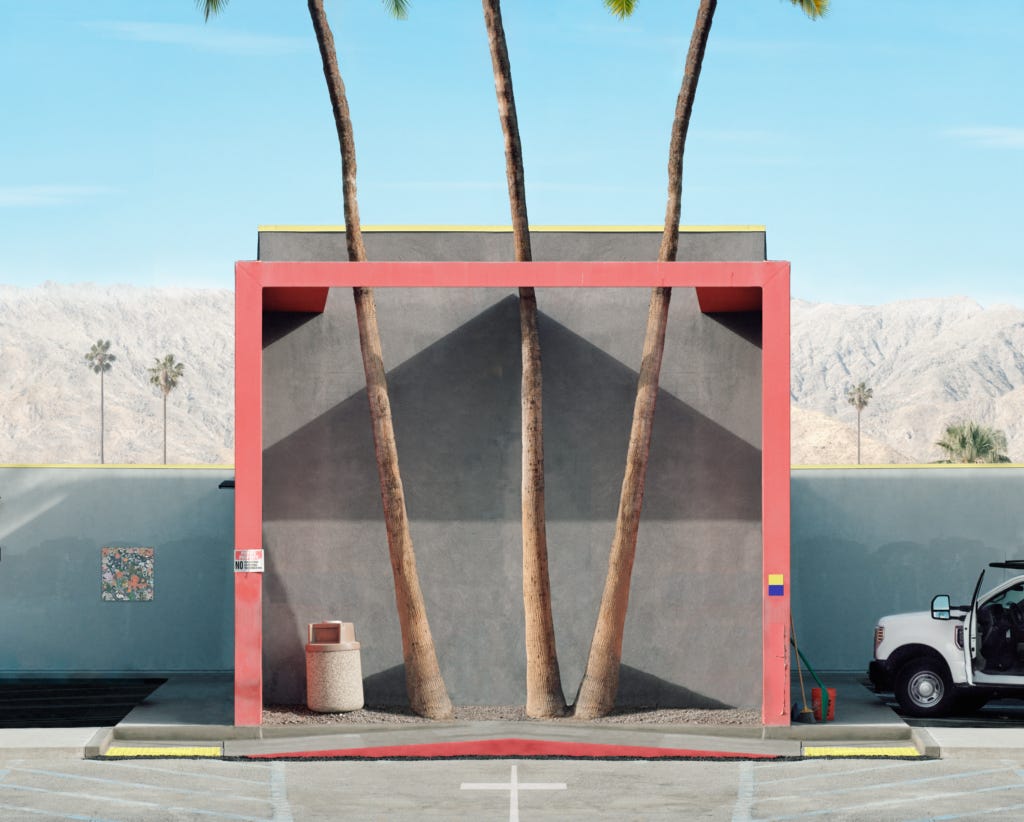 Modern architecture with palm trees framed by a vibrant red border, van parked nearby, mountains in background.