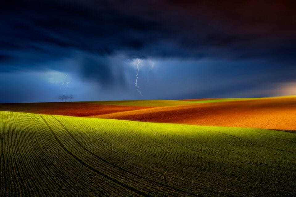 Vivid landscape with colorful fields under a stormy sky, highlighted by lightning in the distance.