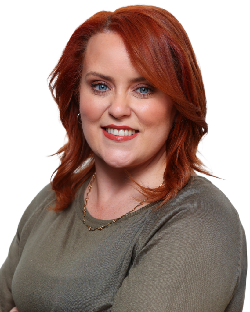 Portrait of a smiling person with red hair wearing a green top and gold necklace.