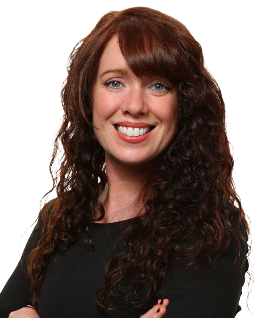 Smiling woman with long, curly brown hair wearing a black top, arms crossed against a white background.