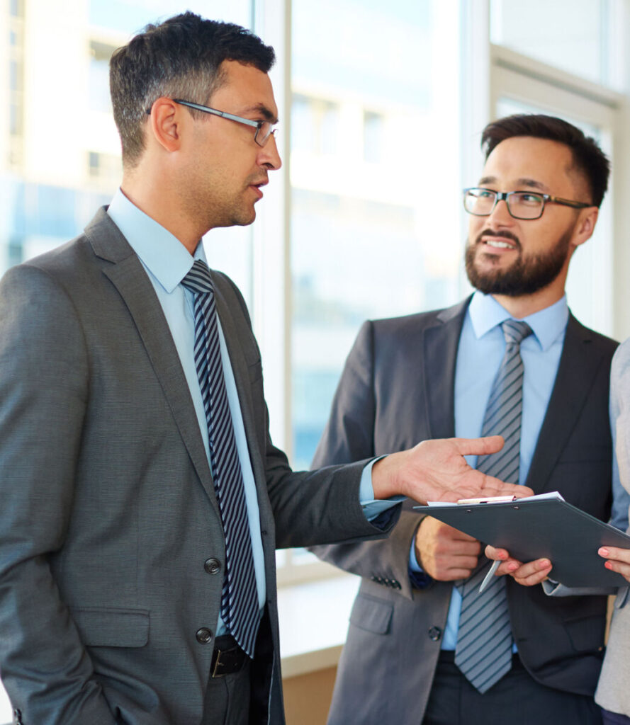 Two business professionals in suits discussing documents in a bright office setting.