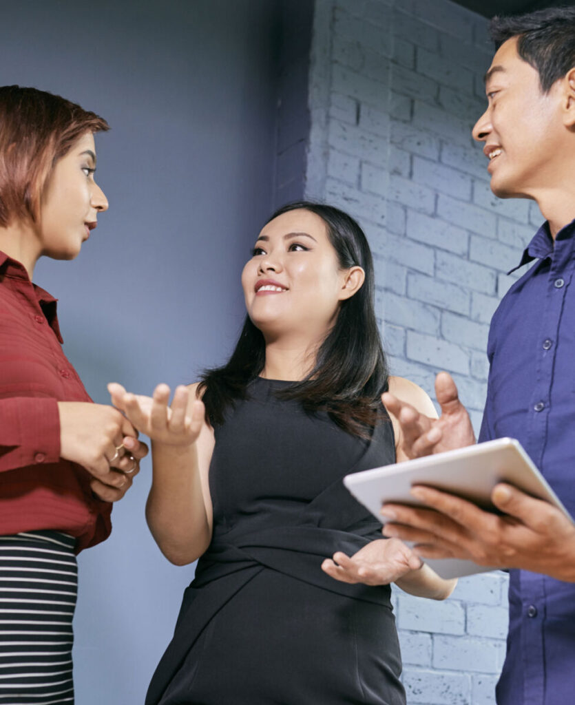 Three people engaging in a lively discussion, with one holding a tablet, in a modern office setting.
