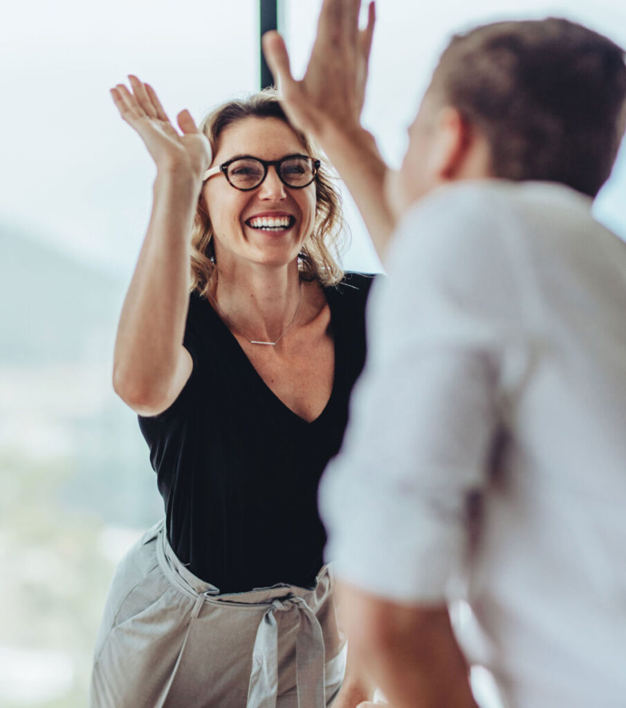 Two people celebrating with a high-five, woman in glasses smiling, bright office background.