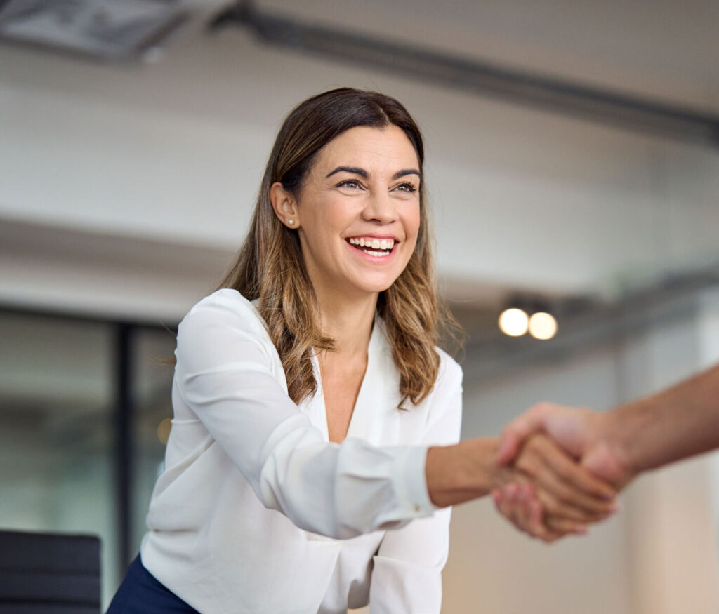 Smiling woman in white blouse shaking hands, in a professional setting.